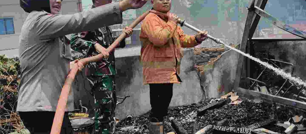 Bu Bhabin Bhabinkamtibmas Polsek Bangko mengangkat selang saat membantu pemadaman kebakaran di Kota Bangko